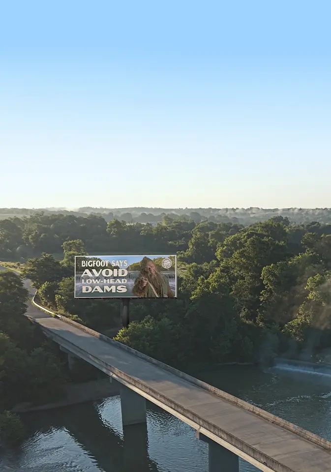Overhead view of a river and bridge with a Bigfoot dam safety billboard