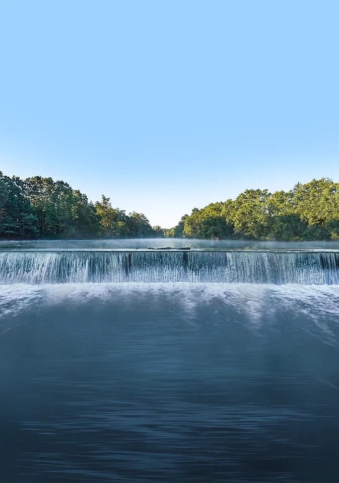 Low-head dam waterfall on a misty tree-lined river